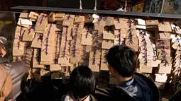 Pelajar melihat papan Ema berisi harapan di Kuil Yushima Tenmangu, Tokyo, Jepang, (7/1). Para siswa dan orang tua di Tokyo ramai-ramai mengunjungi Kuil Yushima Tenmangu untuk berdoa sebelum ujian sekolah dimulai. (AFP Photo/Kazuhiro Nogi)