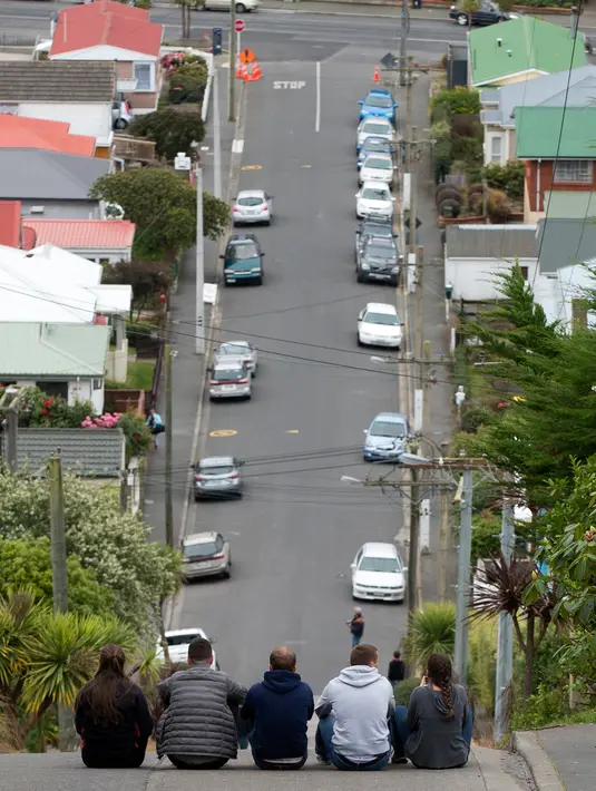 Wisatawan duduk di tengah jalanan paling curam di dunia, Baldwin Street, di kota Dunedin, Selandia Baru, 26 Agustus 2017. Jalan curam ini sendiri sebenarnya merupakan efek dari perencanaan pembangunan yang salah. (AP Photo/Mark Baker)