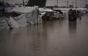 Warga Palestina menyeberangi jalan yang tergenang banjir setelah hujan lebat di Khan Younis, Jalur Gaza selatan, Kamis 11 Desember 2025. Hujan deras di Khan Younis menyebabkan kondisi kemanusiaan di kamp-kamp pengungsi menjadi sangat kritis. (AP Photo/Abdel Kareem Hana)