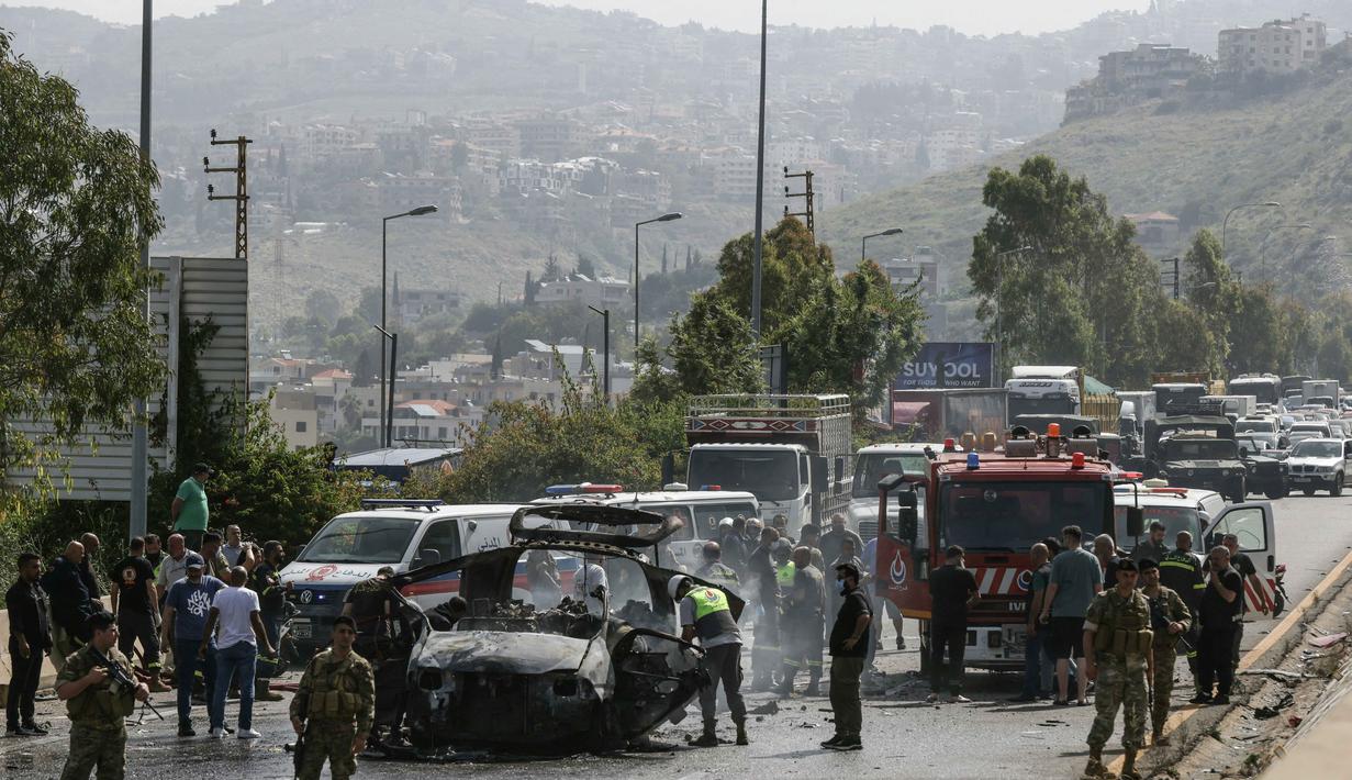 Petugas tanggap darurat bekerja di sekitar kendaraan yang menjadi sasaran serangan pesawat tak berawak Israel di jalan raya dekat kota Jiyeh, Selatan Beirut, pada Rabu 13 Mei 2026. (MAHMOUD ZAYYAT/AFP)