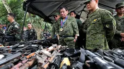 Presiden Filipina, Rodrigo Duterte meninjau ratusan pucuk senjata yang berhasil disita oleh tentara Filipina sejak konflik di Marawi, Kamis (20/7). Duterte melakukan kunjungan mendadak ke medan pertempuran dengan terbang menumpang helikopter (AP Photo)