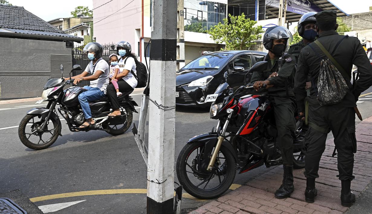 Para komuter melewati tentara yang berjaga di sepanjang jalan di Kolombo pada Sabtu (2/4/2022). Pasukan yang dipersenjatai dengan senapan serbu otomatis dikerahkan di Sri Lanka untuk mengendalikan massa, beberapa jam setelah presiden menyatakan keadaan darurat. (KODIKARA / AFP)