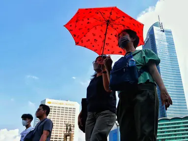 Warga menggunakan payung saat berjalan di tengah cuaca terik di kawasan Bundaran HI, Jakarta, Senin (24/4/2023). Badan Meteorologi Klimatologi dan Geofisika (BMKG) menyampaikan dinamika atmosfer yang tidak biasa menjadi salah satu penyebab Indonesia mengalami suhu panas dalam bebrapa hari terakhir. (Liputan6.com/Angga Yuniar)