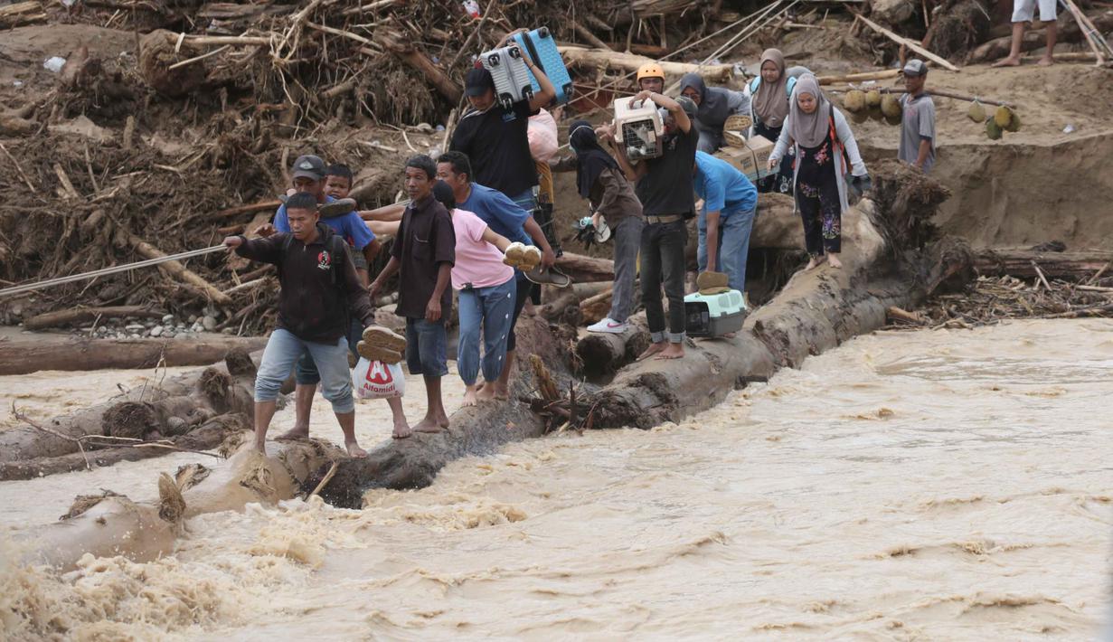 Inisiatif membuat jembatan darurat dari kayu gelondongan ini merupakan upaya relawan dan masyarakat setempat agar aktivitas dan penyaluran bantuan dapat dilakukan. Tampak dalam foto, warga yang menjadi korban banjir menggunakan kayu gelondongan untuk menyeberangi sungai di Batang Toru, Sumatra Utara, Selasa 2 Desember 2025. (AP Photo/Binsar Bakkara)