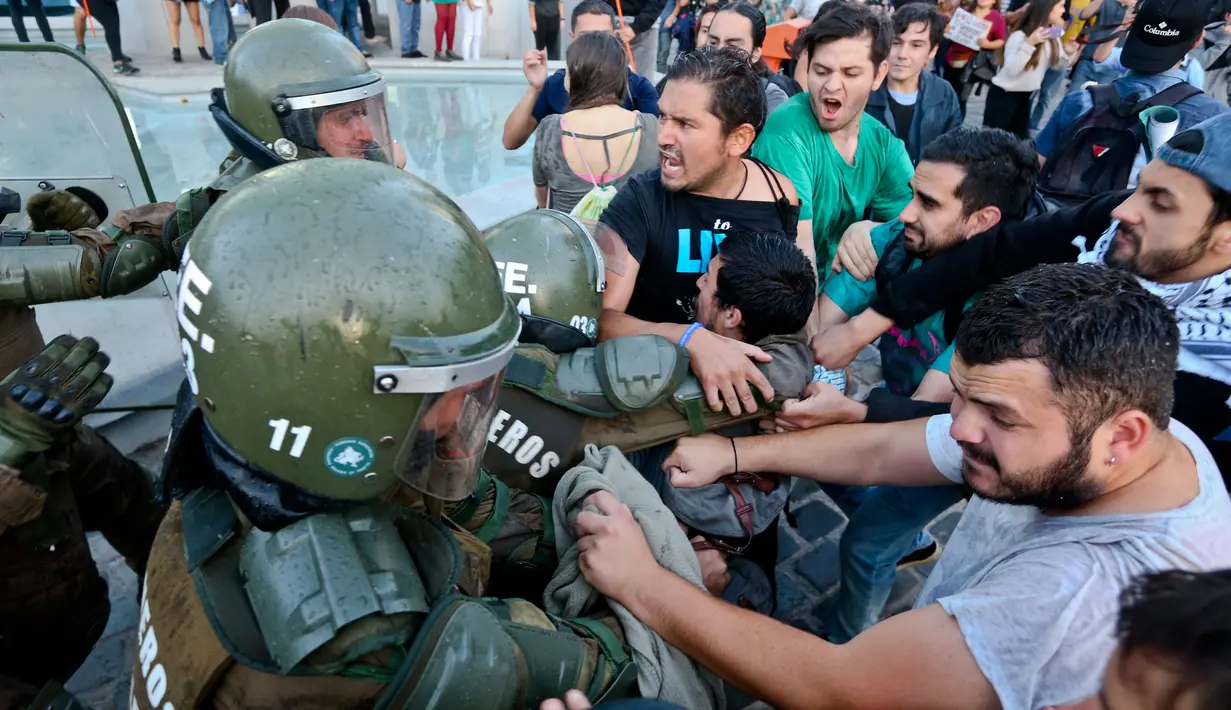 Para pengunjuk rasa mencoba membebaskan rekannya yang ditahan oleh polisi anti huru hara saat demonstrasi di luar kedutaan AS di Santiago, Chili (14/4). Mereka melakukan aksi menentang serangan AS ke Suriah. (AP / Esteban Felix)