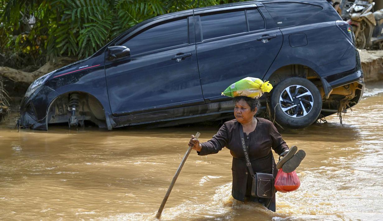 Bupati Tapanuli Tengah, Masinton Pasaribu melalui akun media sosialnya mengungkap identitas 86 orang meninggal dunia akibat banjir bandang dan longsor. Ia juga menjelaskan, ada 508 orang terluka, 7.382 orang mengungsi dan 296.454 orang terdampak bencana ini. Tampak dalam foto, seorang perempuan mengarungi banjir bandang di Desa Tukka, Tapanuli Tengah, Sumatera Utara, pada 2 Desember 2025. (YT HARIONO/AFP)