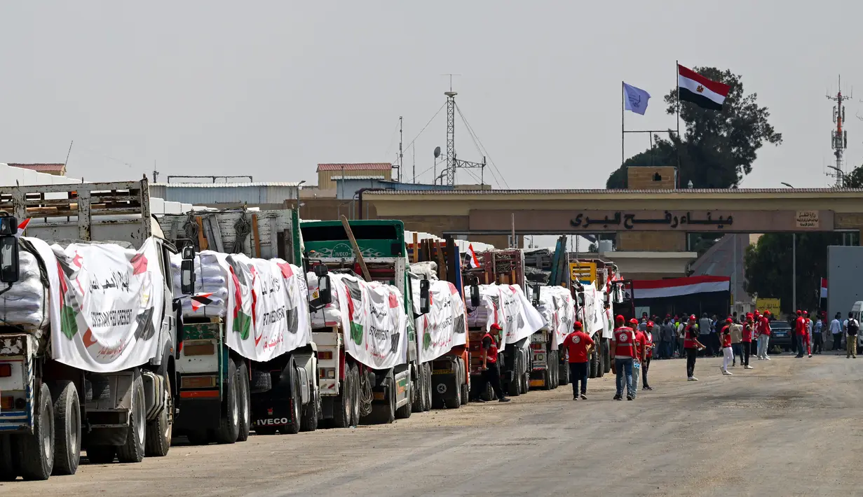 Orang-orang berjalan melewati truk-truk yang dimuat dengan bantuan untuk Gaza, menunggu di sisi Mesir dari pos perbatasan Rafah pada 18 Agustus 2025. (Khaled DESOUKI/AFP)