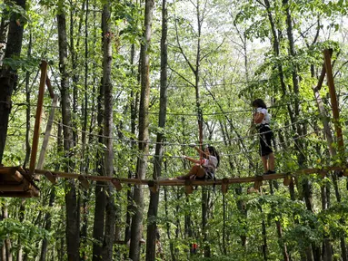 Pengunjung melintasi jalan setapak antarpepohonan di Edenland Park, Balotesti, Rumania, Rabu (4/10/2023). Edenland Park merupakan tempat petualangan terbesar di Rumania. (Liputan6.com/Herman Zakharia)