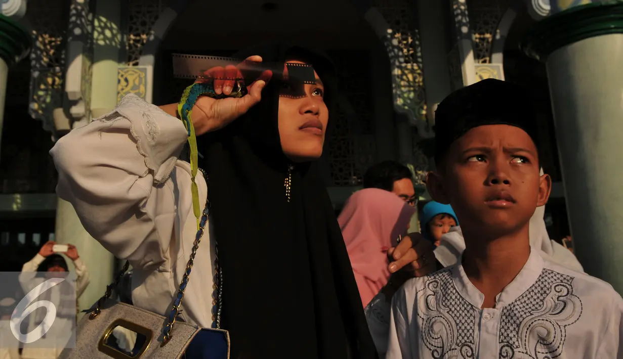 Warga menikmati proses Gerhana Matahari Total (GMT) menggunakan film bekas di halaman masjid Al-azhom Kota Tangerang, Rabu (9/3/2016). Salat gerhana tersebut diadakan sebagai ungkapan syukur atas kuasa Allah SWT. (Liputan6.com/Faisal R Syam)
