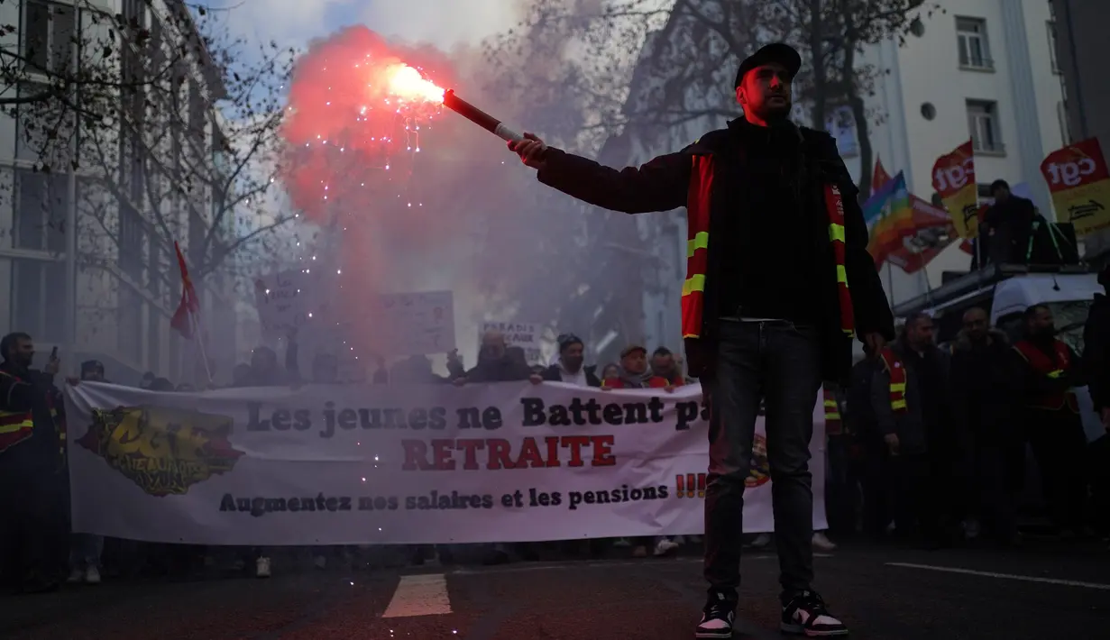 Demonstran dari serikat pekerja CGT yang mengenakan jaket pekerja kereta api memegang suar selama pawai protes, di Lyon, Prancis tengah, Paris, Selasa (31/1/2023). Unjuk rasa yang disertai aksi mogok massal ini diprediksi melumpuhkan sistem transportasi Prancis, terutama kereta. (AP Photo/Laurent Cipriani)