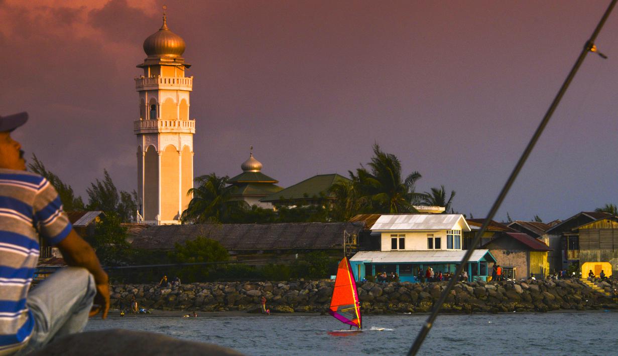 Seorang pria memancing ketika pemain selancar angin melintas saat matahari terbenam di pantai di Banda Aceh (7/4). Sebagai pusat pemerintahan, Banda Aceh menjadi pusat kegiatan ekonomi, politik, sosial dan budaya. (AFP Photo/Chaideer Mahyuddin)