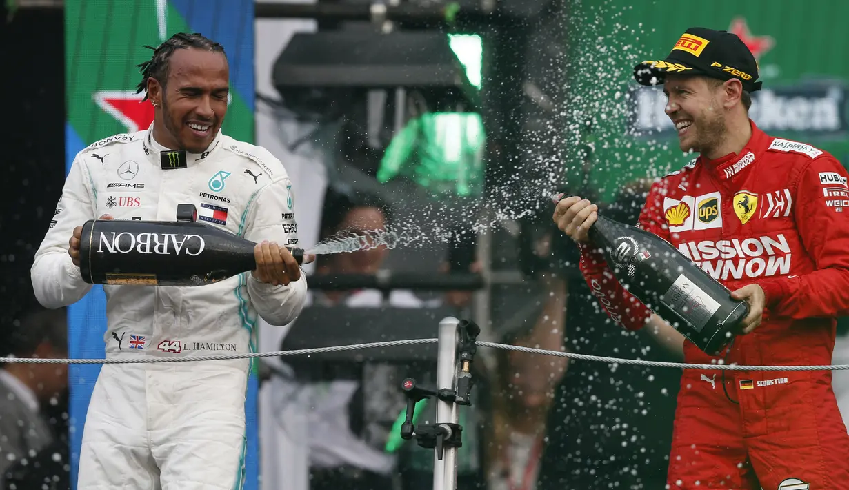 Pembalap Mercedes Lewis Hamilton, menyemprotkan sampanye ke arah pembalap Ferrari Sebastian Vettel setelah berhasil menjuarai balapan GP Meksiko di Autodromo Hermanos Rodriguez, Mexico City (28/10/2019). (AP Photo/Rebecca Blackwell)