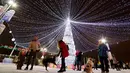 Pengunjung bermain dengan anjing di samping pohon tahun baru dengan dekorasi untuk menyambut Natal 2018 dan Tahun Baru 2019 di Octyabrskaya Square, Minsk, Belarus, Selasa (18/12). (AP Photo/Sergei Grits)