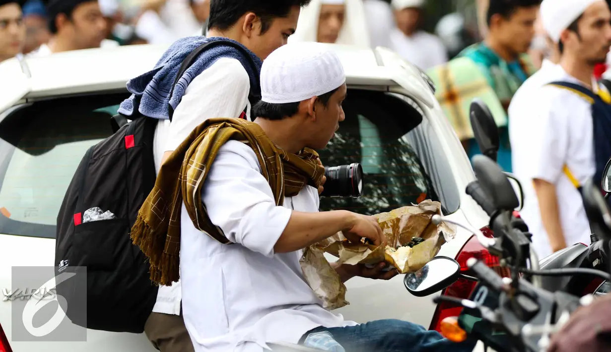 Seorang pengunjuk rasa makan siang diantara kerumunan massa sebelum memulai aksi di Medan Merdeka Timur, Jakarta, Jumat (4/11). (Liputan6.com/Faizal Fanani)