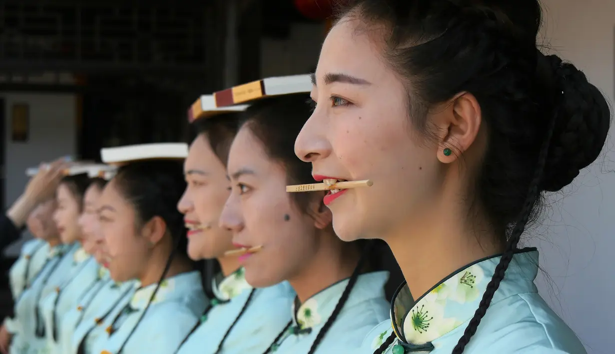 Sejumlah pemandu wisata dari  Slender West Lake scenic menggunakan buku dan sumpit saat mengikuti pelatihan etiket untuk Hari Pariwisata China (18/5). Pelatihan ini untuk menguji keseimbangan tubuh. (AFP Photo/Str/China Out)