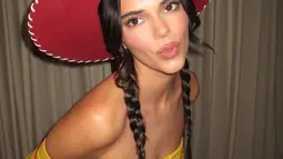 Kendall Jenner memamerkan perutnya yang kencang dalam balutan kemeja putih bergaya kartun dengan kerah besar, kancing, dan detail manset kuning. (Instagram/Kendalljenner)