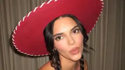 Kendall Jenner memamerkan perutnya yang kencang dalam balutan kemeja putih bergaya kartun dengan kerah besar, kancing, dan detail manset kuning. (Instagram/Kendalljenner)