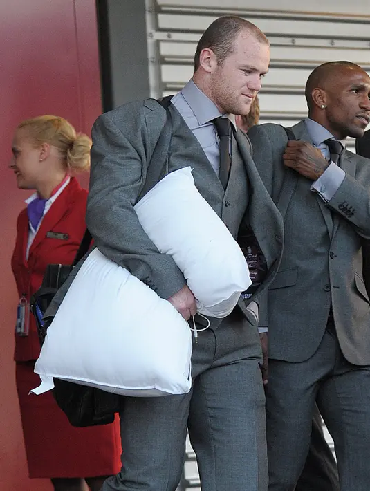 Penyerang Inggris, Wayne Rooney membawa sebuah bantal sebelum menaiki pesawat di bandara Heathrow, London pada 2 Juni 2010. (AFP PHOTO / CARL DE SOUZA)