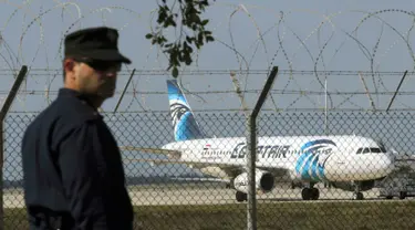 Seorang polisi berjaga di dekat pesawat milik maskapai Mesir, EgyptAir, yang dibajak dan dipaksa mendarat di Bandara Larnaca, Siprus, Selasa (29/3). Pembajak adalah seorang penumpang yang mengklaim membawa sabuk bahan peledak. (REUTERS/Yiannis Kourtoglou)