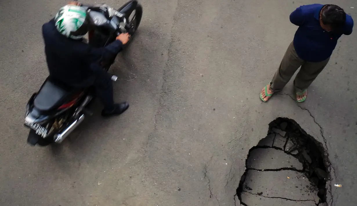 Salah satu warga dan pengendara motor memperhatikan kondisi sebagian ruas jalan yang amblas di depan Wisma Bakrie, Kuningan, Jakarta, (12/8/2014). (Liputan6.com/Faizal Fanani)