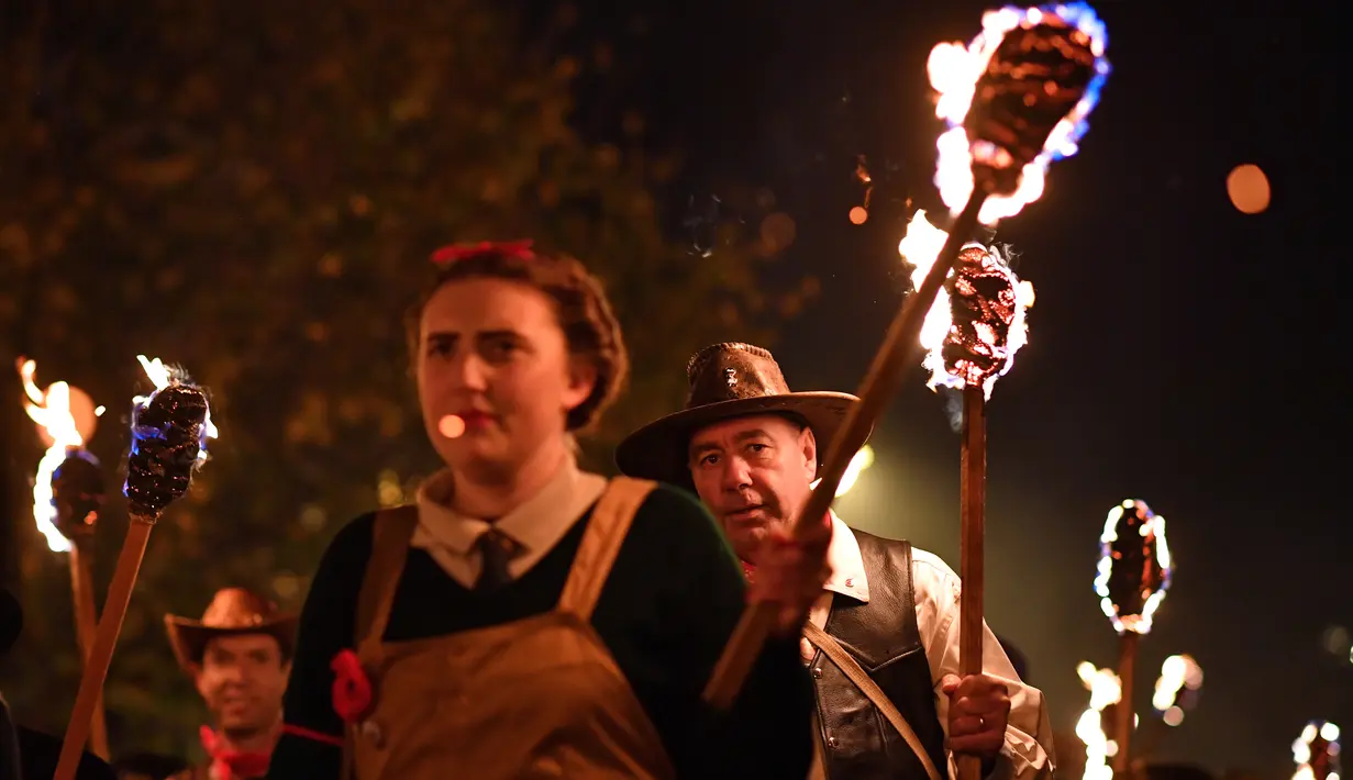 Peserta melakukan pawai sambil membawa obor dalam perayaan Bonfire Night melintasi jalan di Sussex Timur, Inggris, Selasa (5/11/2019). Tak hanya itu, penduduk Inggris juga akan membawa patung berukuran besar dan mengaraknya sembari berparade. (Ben STANSALL/AFP)