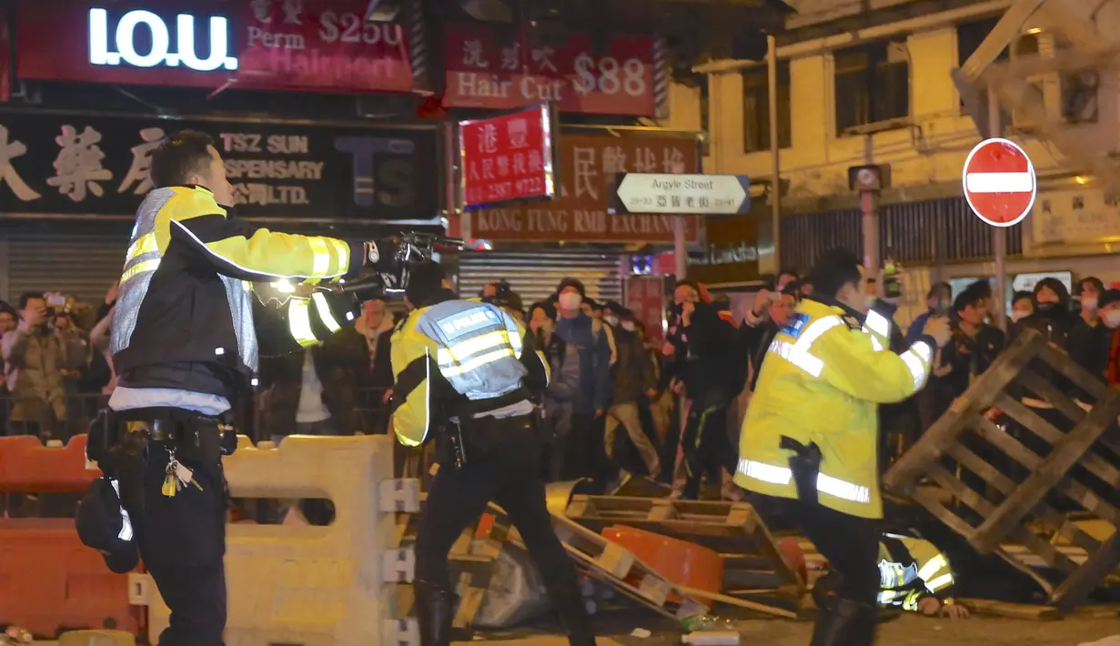 Petugas polisi (kiri) mengeluarkan pistol saat bentrok dengan sejumlah pengunjuk rasa di Mongkok, Hong Kong, Selasa (9/2). Bentrokan dimulai ketika pemerintah daerah mencoba untuk menertibkan PKL yang beroperasi. (REUTERS/E Weekly/Fu Chun-wai)