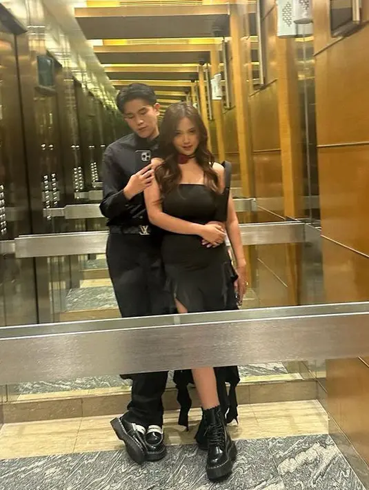 Julian Jacob tampil dengan kemeja lengan panjang dan celana panjang hitam serasi dengan istrinya, Marriam Eka yang mengenakan tube dress hitam  asimetris dengan kaung mawarnya. [@julianjacs]