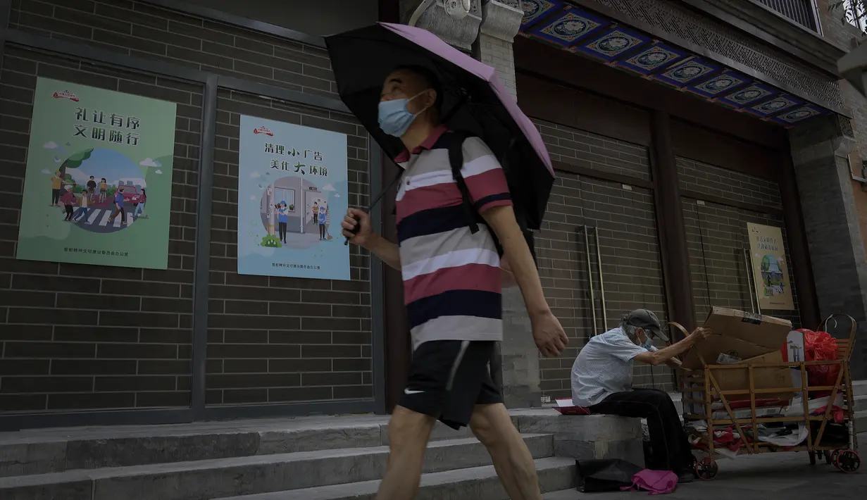 Seorang pria bermasker dan memegang payung saat berjalan melewati seorang pria tua yang mengumpulkan barang-barang daur ulang di depan toko-toko kosong di Qianmen Street di Beijing, Rabu, 17 Agustus 2022. Pabrik-pabrik di barat daya China telah ditutup dan sebuah kota memberlakukan pemadaman bergilir setelah waduk yang digunakan untuk menghasilkan tenaga air mulai menipis akibat kekeringan yang memburuk. (AP Photo/Andy Wong)