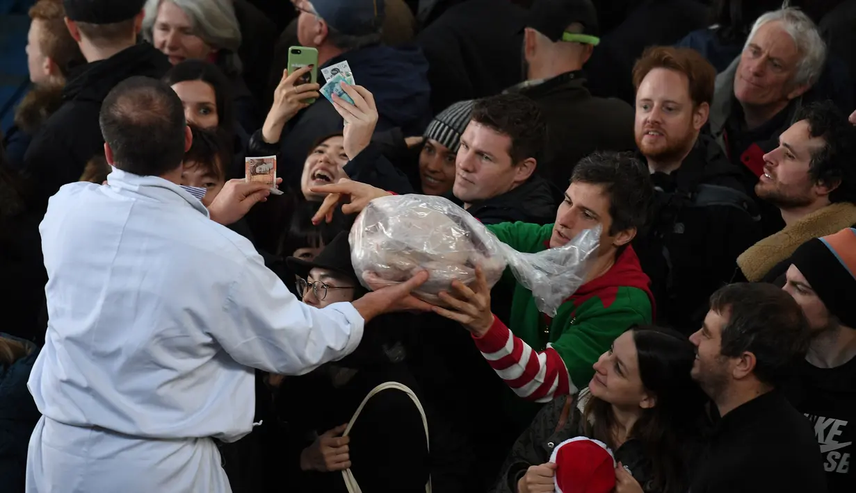 Seorang penjual memberikan daging kepada pembeli selama lelang tahunan menyambut malam Natal di Smithfield Market, London, Selasa (24/12/2019). Operasi pasar ini menjadi sarana menghabiskan persediaan para pemilik toko jelang tahun baru. (DANIEL LEAL-OLIVAS / AFP)