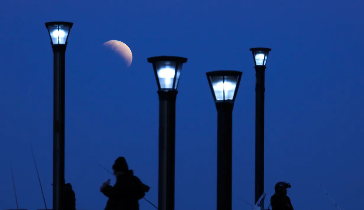 Sejumlah pria berdiri di bawah lampu jalan ketika fenomena gerhana bulan sebagian (parsial) di Buenos Aires, Argentina, Selasa (16/7/2019). Gerhana bulan parsial ini bisa diamati dari Amerika Selatan, Eropa, Afrika, Asia dan Australia. (AP Photo/Natacha Pisarenko)