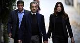 Mantan Presiden Prancis Nicolas Sarkozy (tengah), bersama istrinya Carla Bruni-Sarkozy, berjalan meninggalkan kediamannya untuk menyerahkan diri ke Penjara La Sante guna menjalani hukuman penjara lima tahun setelah dinyatakan bersalah atas konspirasi kriminal terkait rencana pendanaan kampanye pemilu 2007-nya oleh diktator Libya Moamer Kadhafi, di Paris, pada 21 Oktober 2025. (JULIEN DE ROSA/AFP)
