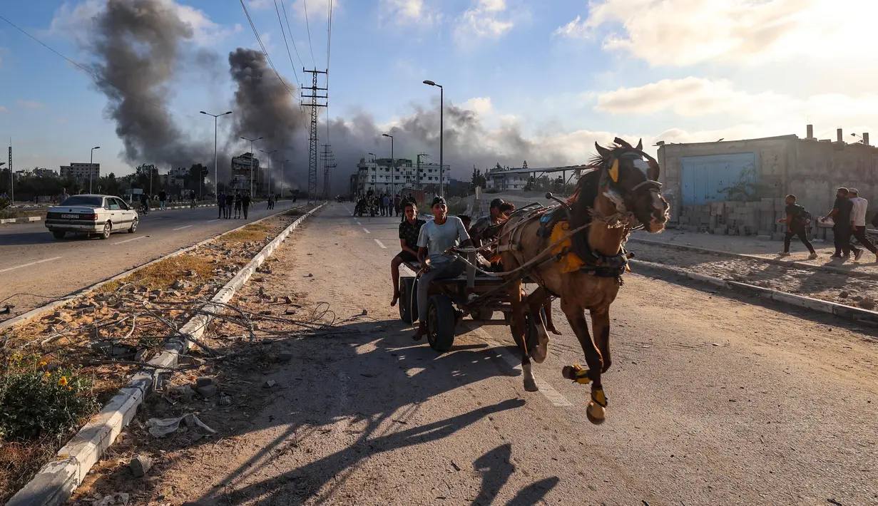 Gumpalan asap hitam membumbung tinggi selama serangan Israel ketika warga Palestina yang mengendarai gerobak yang ditarik kuda melaju di sepanjang jalan Salah al-Din di dekat kamp pengungsi Nusseirat, Jalur Gaza Tengah, pada 25 Juni 2025. (Eyad BABA/AFP)