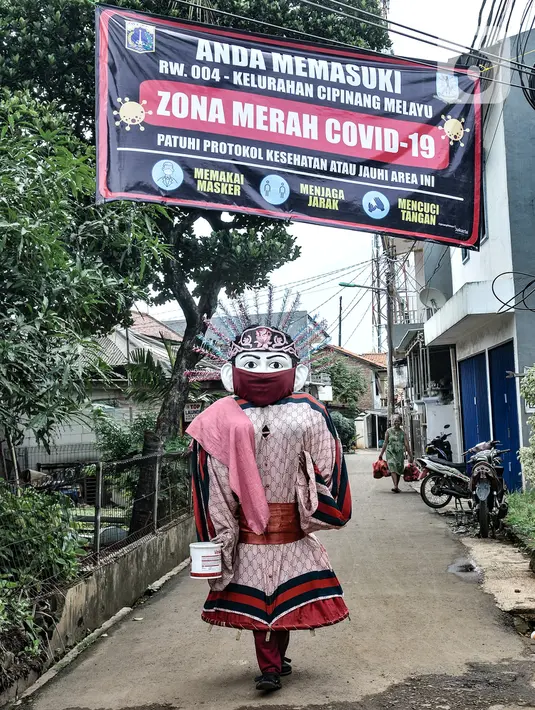 Ondel-ondel berjalan di dekat spanduk peringatan Zona Merah di RW 004, Kelurahan Cipinang Melayu, Kecamatan Makassar Jakarta, Rabu (27/1/2021). Pemprov DKI Jakarta mencatat sebanyak 54 rukun warga (RW) menjadi zona merah Covid-19 per 21 Januari 2021. (merdeka.com/Iqbal S Nugroho)