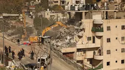 Para aktivis menyebutnya sebagai pembongkaran terbesar di area tersebut tahun ini. Tampak dalam foto, pasukan keamanan Israel berkumpul saat ekskavator merobohkan sebuah bangunan yang dibangun tanpa izin di daerah Wadi Qaddum dekat lingkungan Silwan di Yerusalem timur pada Senin 22 Desember 2025. (Ahmad GHARABLI/AFP)