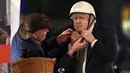 Perdana Menteri Inggris Boris Johnson (kanan) menerima bantuan saat ia mengenakan helm sebelum mengendarai sepeda saat kunjungannya ke pasar Makanan dan Minuman Inggris yang didirikan di Downing Street, London, 30 November 2021. Ada 12 bisnis dari seluruh Inggris. (JUSTIN TALLIS/AFP/POOL)