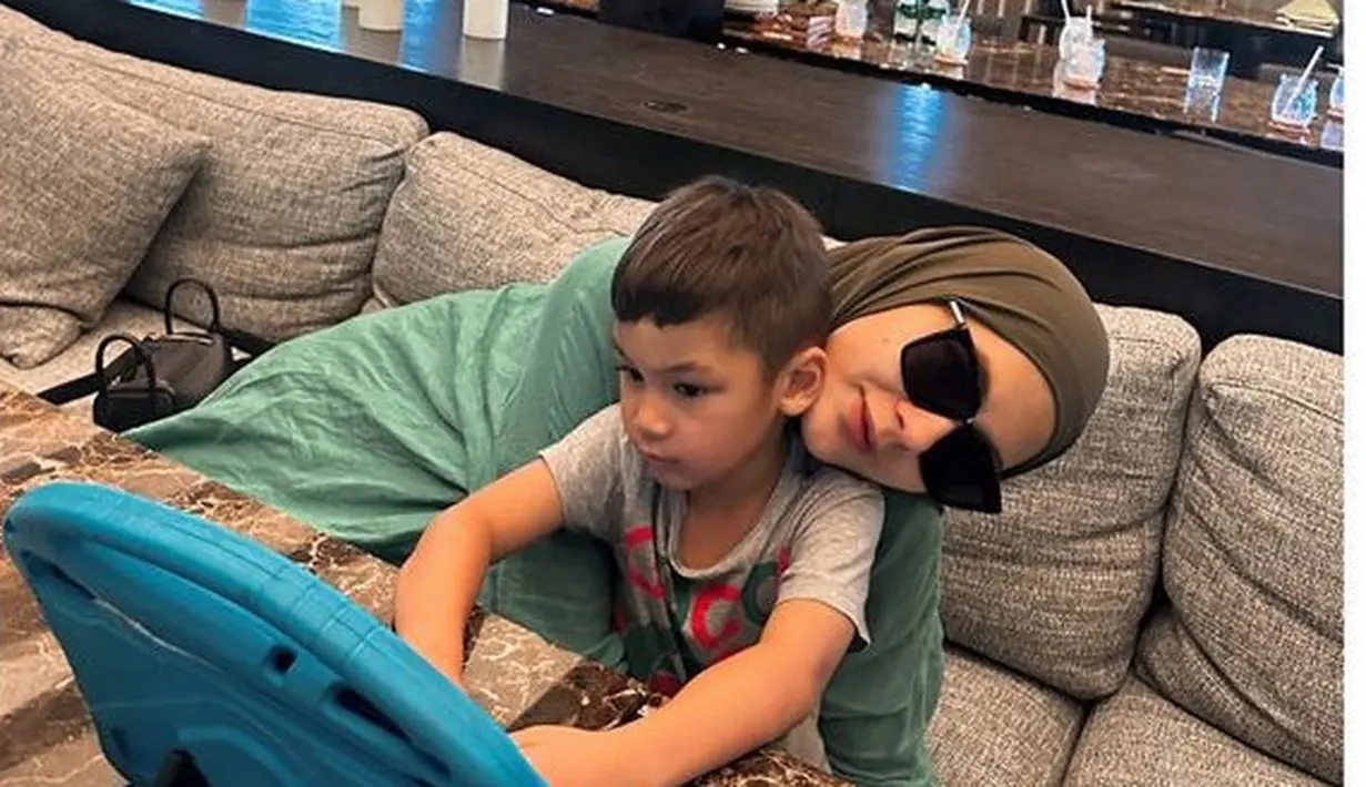 Paula Verhoeven yang mengenakan kemeja hijau dipadukan kerudung warna hijau army mengajak putranya liburan ke Semarang. Ia pun lengkap mengenakan kacamata hitamnya. [@paula_verhoeven]