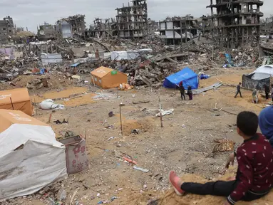 Anak-anak Palestina yang mengungsi duduk di atas gundukan pasir yang menghadap ke tenda-tenda yang didirikan di tengah-tengah bangunan yang hancur di Jabalia, Jalur Gaza utara pada 6 Februari 2025, saat gencatan senjata dalam perang antara Israel dan Hamas. (Bashar TALEB/AFP)