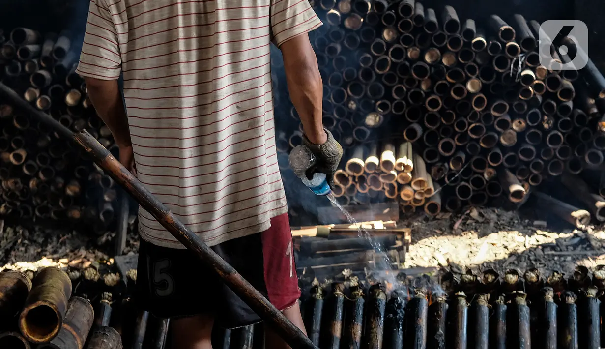 Pekerja menyemprotkan minyak saat membakar lemang yang sudah dibungkus daun pisang dan dimasukkan ke dalam bambu di industri pembuatan lemang kawasan Senen, Jakarta, Selasa (27/4/2021). Pemilik industri mengaku menurunkan jumlah produksi karena penjualan yang cukup sulit. (Liputan6.com/Johan Tallo)