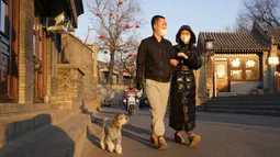 Warga yang mengenakan masker berjalan dengan anjing mereka di Beijing, China, Selasa (11/1/2022). Beijing dalam siaga tinggi menjelang Olimpiade Musim Dingin saat China mengunci kota ketiga di tempat lain akibat COVID-19. (AP Photo/Ng Han Guan)