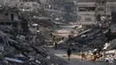 Jabalia, wilayah yang menjadi salah satu kamp pengungsi terbesar dan terpadat di Gaza, mengalami kehancuran infrastruktur yang parah. Tampak dalam foto, orang-orang berjalan di antara bangunan-bangunan yang hancur di Jabalia, di bagian utara Jalur Gaza, Minggu 7 Desember 2025. (AP Photo/Jehad Alshrafi)