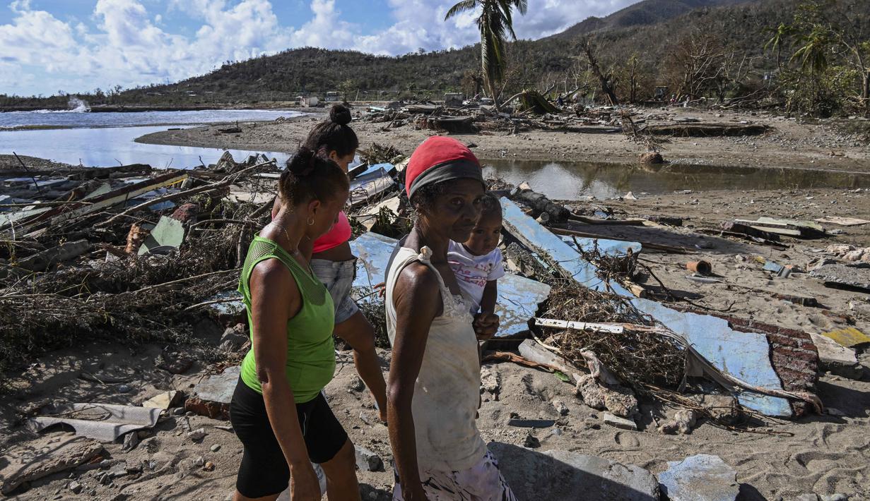 Warga berjalan di tengah puing-puing rumah yang rusak akibat Badai Melissa di desa Boca de Dos Rios, provinsi Santiago de Cuba, Kuba pada Kamis 30 Oktober 2025. Pihak berwenang Kuba juga mengevakuasi lebih dari 735.000 orang dari daerah rawan sebelum badai tiba. (YAMIL LAGE/AFP)