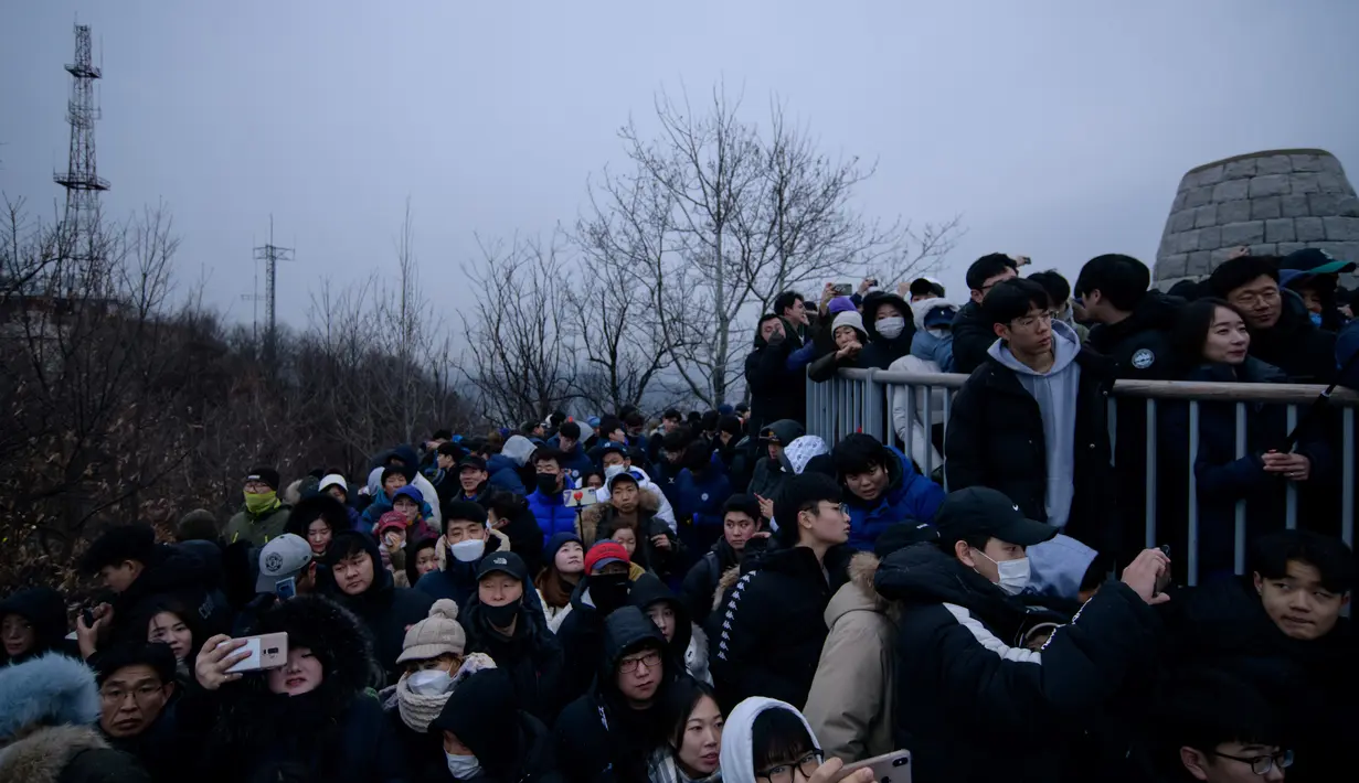 Orang-orang berkumpul di sudut pandang yang menghadap ke cakrawala kota untuk menyaksikan matahari terbit pertama tahun baru, meskipun dalam kondisi mendung, di Seoul, Korea Selatan (1/1/2020). (AFP/Ed Jones)
