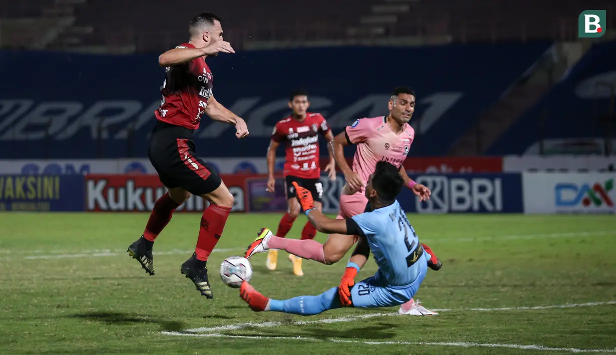 Kiper Madura United, Muhammad Ridho (kanan) berusaha menghalau bola tendangan pemain Bali United, Ilija Spasojevic dalam laga pekan ke-16 BRI Liga 1 2021/2022 di Stadion Sultan Agung, Bantul, Kamis (09/12/2021). (Bola.com/Bagaskara Lazuardi)