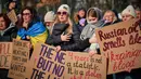 Anggota komunitas Ukraina, termasuk anak-anak dan pengungsi, berkumpul untuk menunjukkan solidaritas dan menuntut keadilan. Tampak dalam foto, orang-orang memegang spanduk saat anggota komunitas Ukraina menggelar protes untuk menandai tahun keempat sejak dimulainya invasi skala penuh Rusia ke Ukraina di Bukares, Rumania, Minggu 22 Februari 2026. (AP Photo/Vadim Ghirda)
