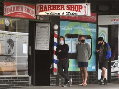 Para pria antre untuk memotong rambut di luar barber shop di Melbourne, Australia, Senin (19/10/2020). Warga Kota Melbourne, pada Senin (19/10), akhirnya bisa bernafas lega saat sejumlah pembatasan dilonggarkan setelah lockdown tahap keempat yang ketat selama sekitar 100 hari. (William WEST/AFP)