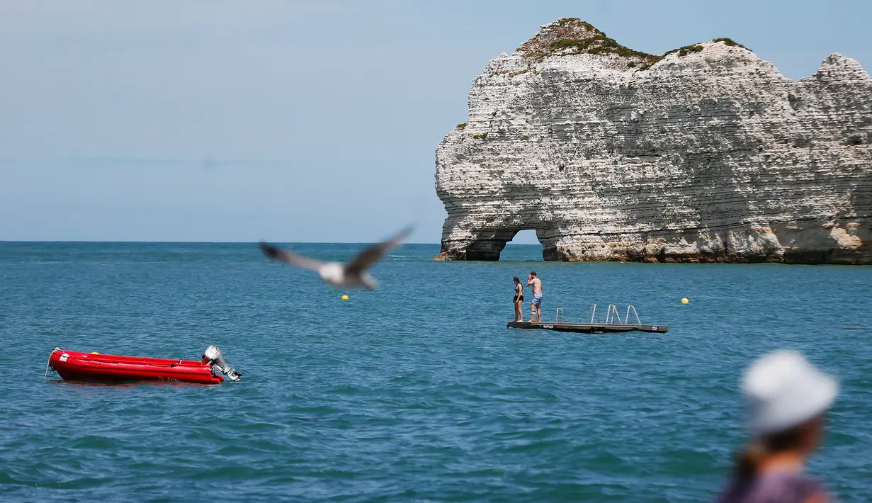 Seekor burung camar terbang di atas perenang di lepas pantai Etretat, Prancis barat laut (17/7). Tebing-tebing dan pantai di Étretat menarik para seniman seperti Eugène Boudin, Gustave Courbet dan Claude Monet. (AFP Photo/Charly Triballeau)