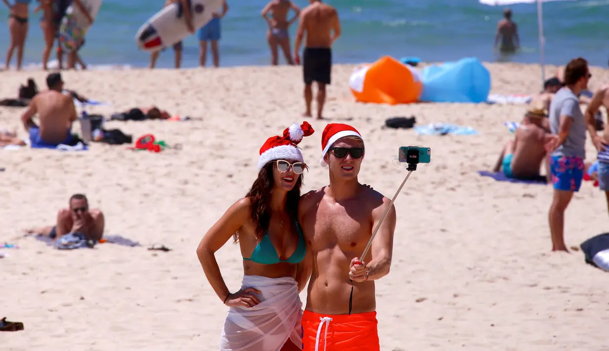 Dua turis mengenakan topi natal berselfie saat merayakan hari Natal di Bondi Beach Sydney pada Hari Natal di Australia, (25/12). (REUTERS/David Gray)