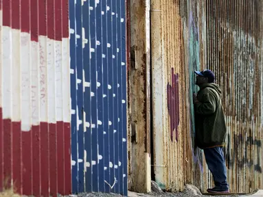 Seorang pria melihat melalui pagar perbatasan Amerika Serikat (AS) dengan Meksiko di Playas de Tijuana, Baja California, Meksiko, Minggu (11/3). Pagar perbatasan terbuat dari struktur baja setinggi sembilan meter. (GUILLERMO ARIAS/AFP)