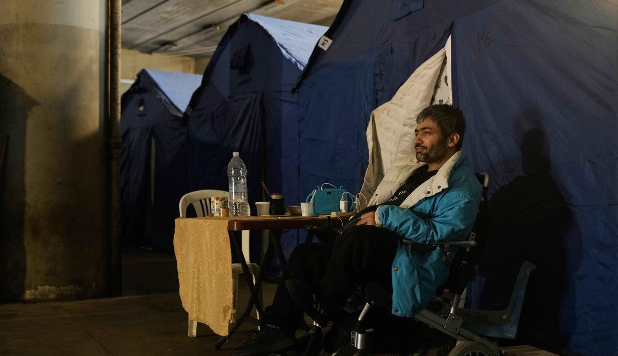 Stadion dengan kapasitas 49.500 hingga 50.000 penonton ini, kini menampung ratusan pengungsi, dengan tenda-tenda yang didirikan di area tersebut. Tampak dalam foto, seorang pria pengungsi duduk di kursi roda listrik di samping tenda-tenda yang didirikan di dalam Camille Chamoun Sports City Stadium, yang telah diubah menjadi tempat penampungan bagi orang-orang yang melarikan diri dari serangan udara Israel di Lebanon selatan, Beirut, Lebanon, Rabu 8 April 2026. (AP Photo/Bilal Hussein)