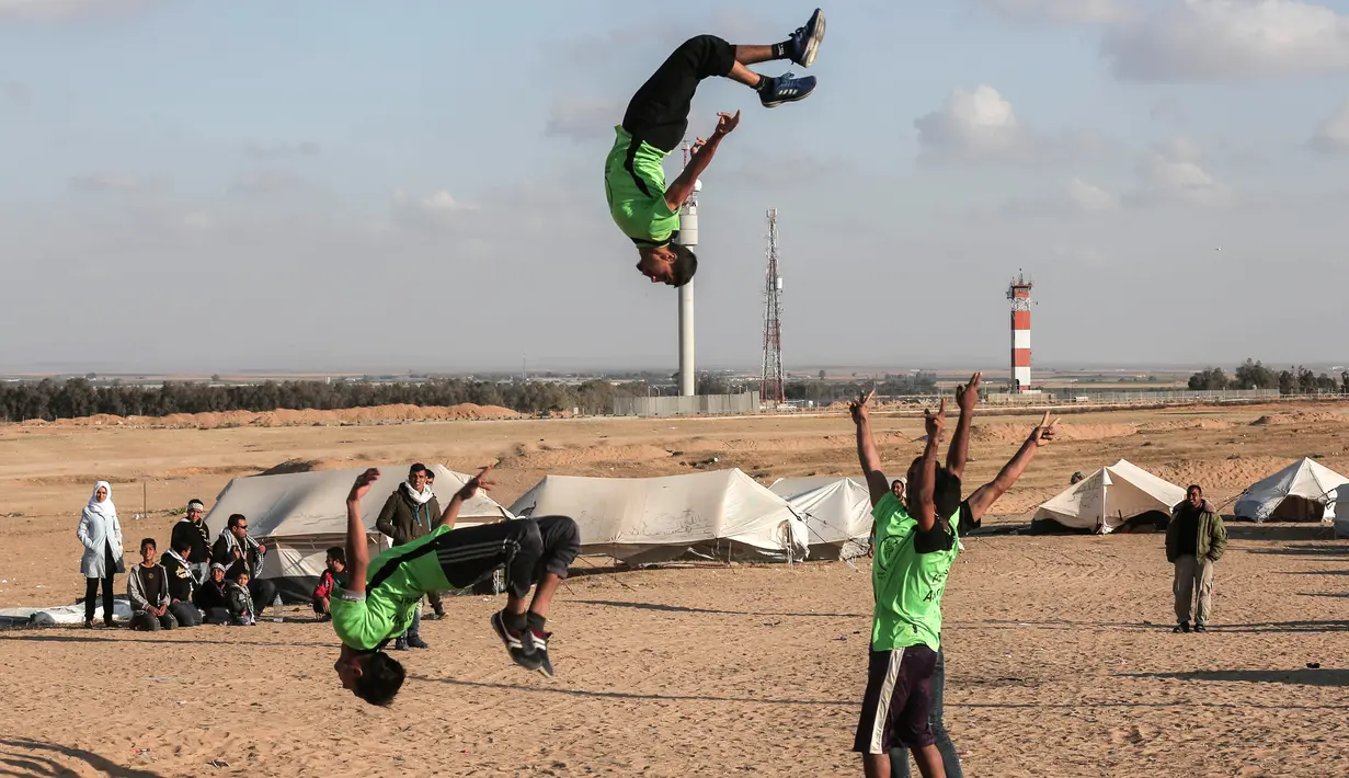 Dua pemuda melompat di udara saat menunjukkan keterampilan parkour mereka di dekat tenda warga di perbatasan Gaza, Palestina (10/4). Mereka menghibur para warga yang melakukan aksi protes di perbatasan Gaza tersebut. (AFP Photo/Said Khatib)